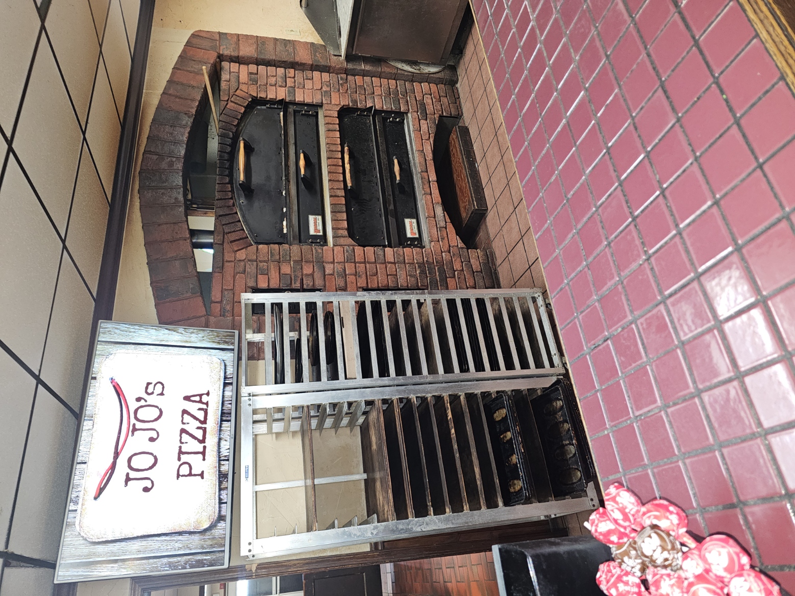 A JoJo's pizzaiolo sliding a fresh cheese pizza into the brick oven on a wooden peel